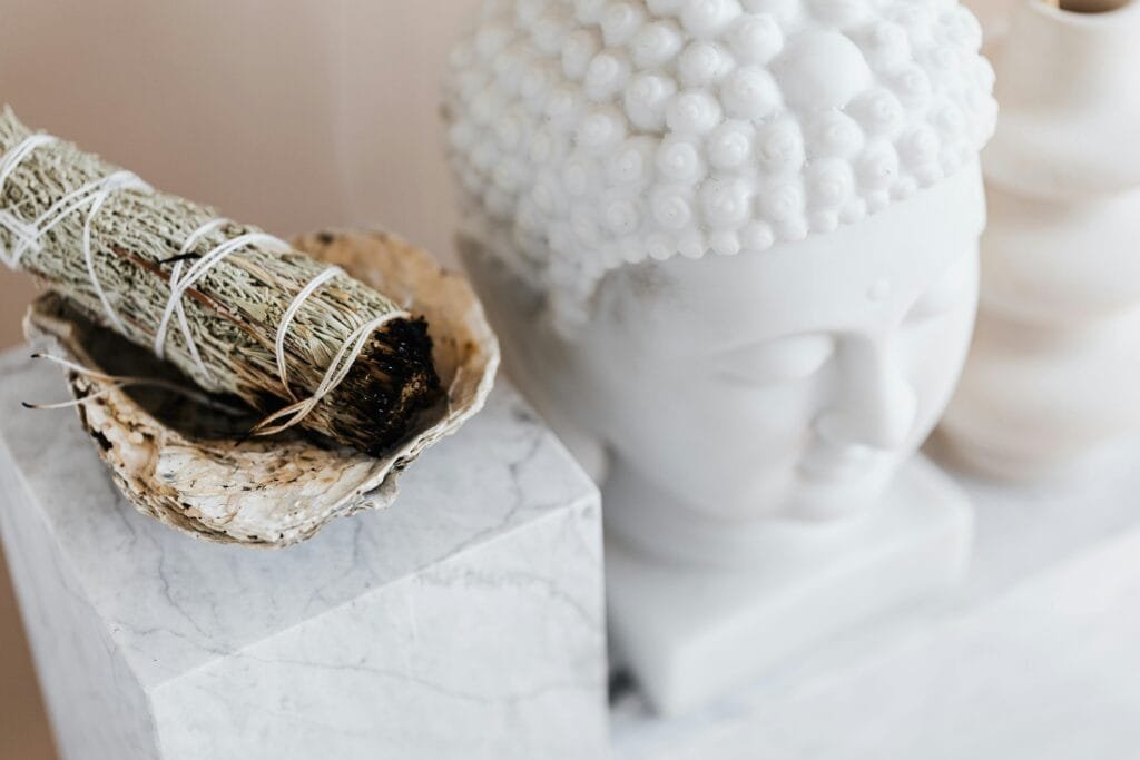 pexels-photo-4203096-4203096 From above of sage candle in bowl placed on white marble shelf near plaster Buddha bust and creative shape vase for home decoration